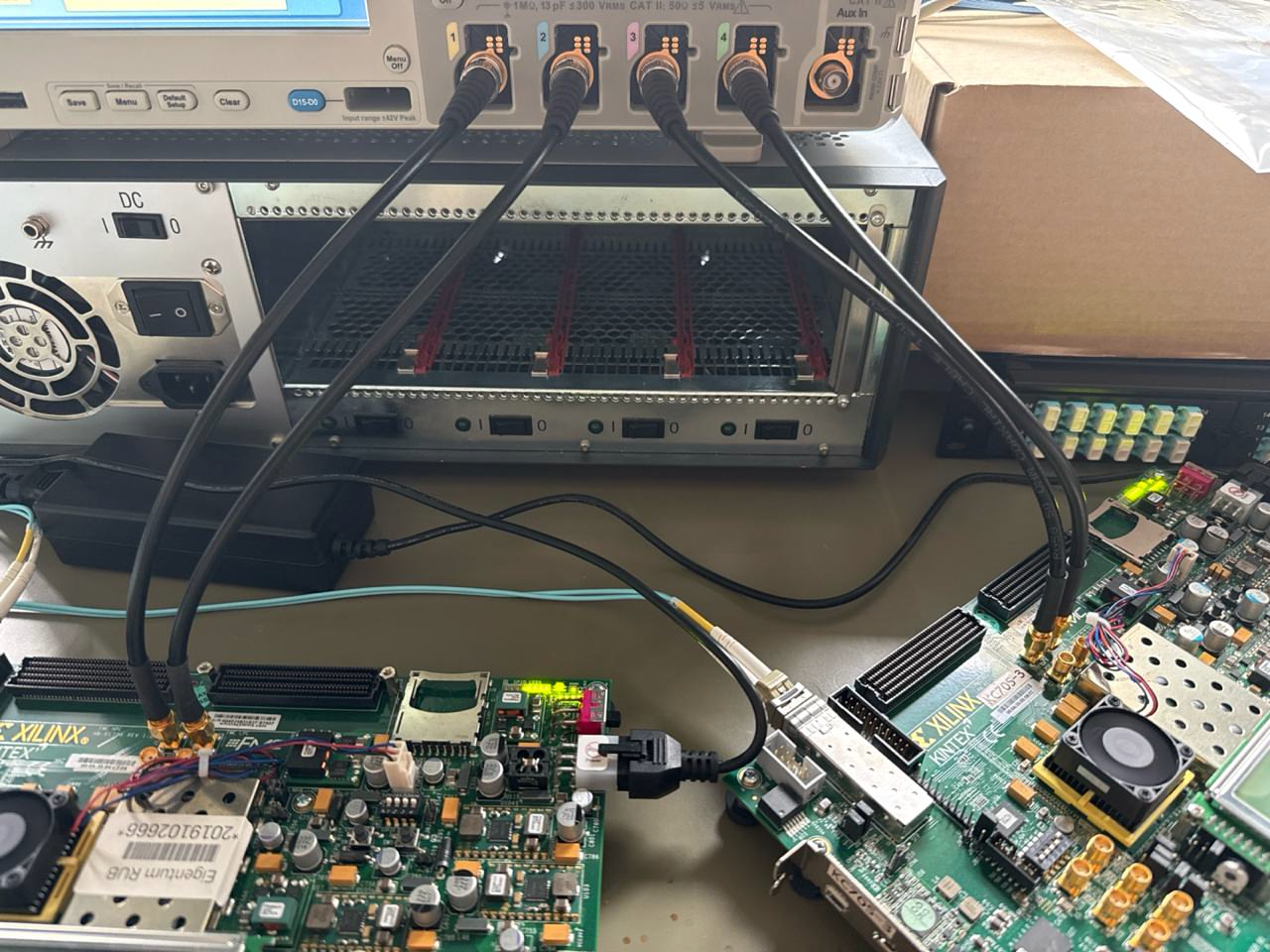 Two Xilinx Kintex-7 development boards connected to an oscilloscope for post-implementation signal verification, used at EP1/RUB for HV-MAPS sensor readout in the PANDA and LHCb experiments