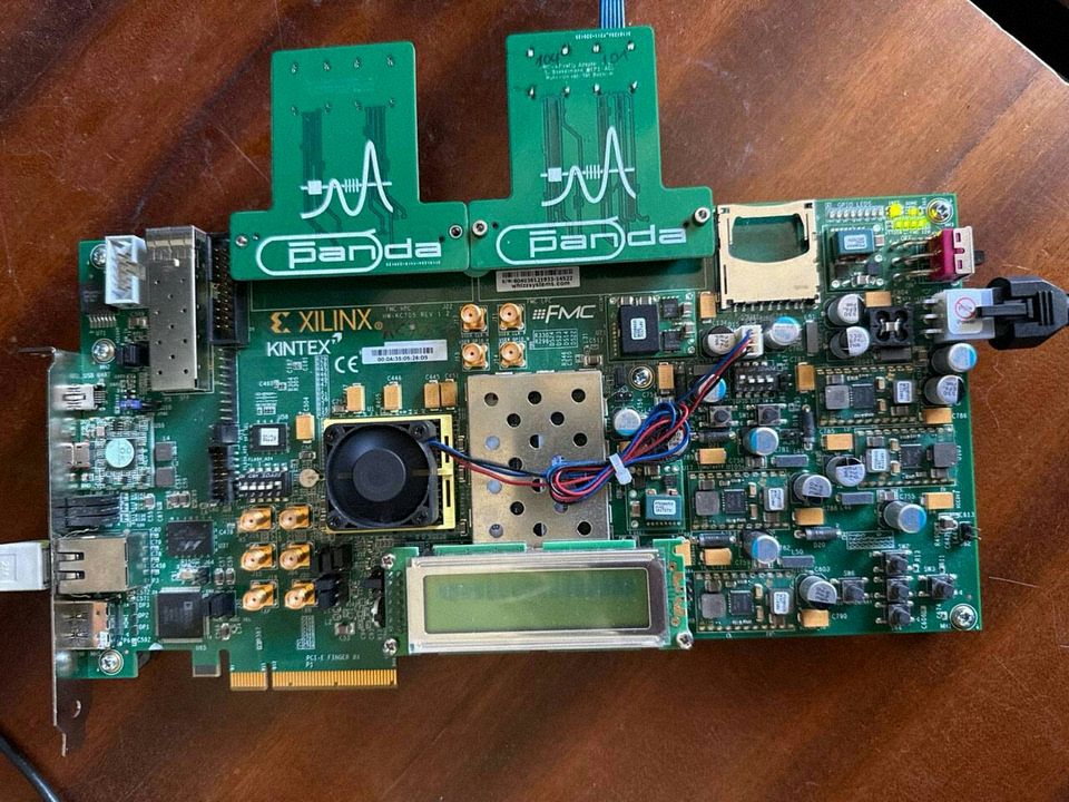 A Xilinx Kintex-7 evaluation board in PCIe form factor, with two Panda FMC mezzanine cards attached, an SFP cage, SMA connectors, and a small cooling fan over the FPGA package