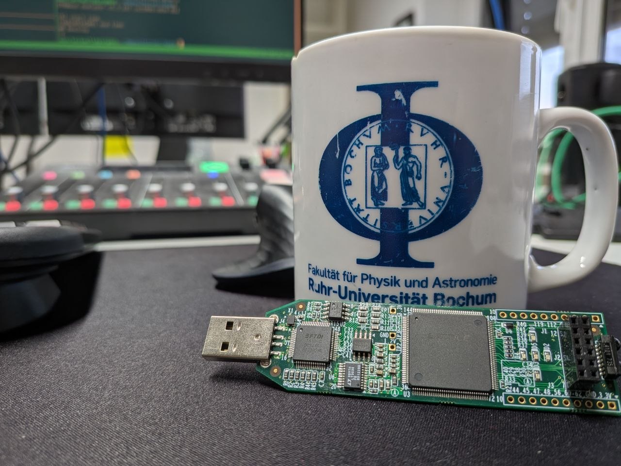 iCEstick leaning against a Ruhr-Universität Bochum physics department mug, mixer and monitor in the background