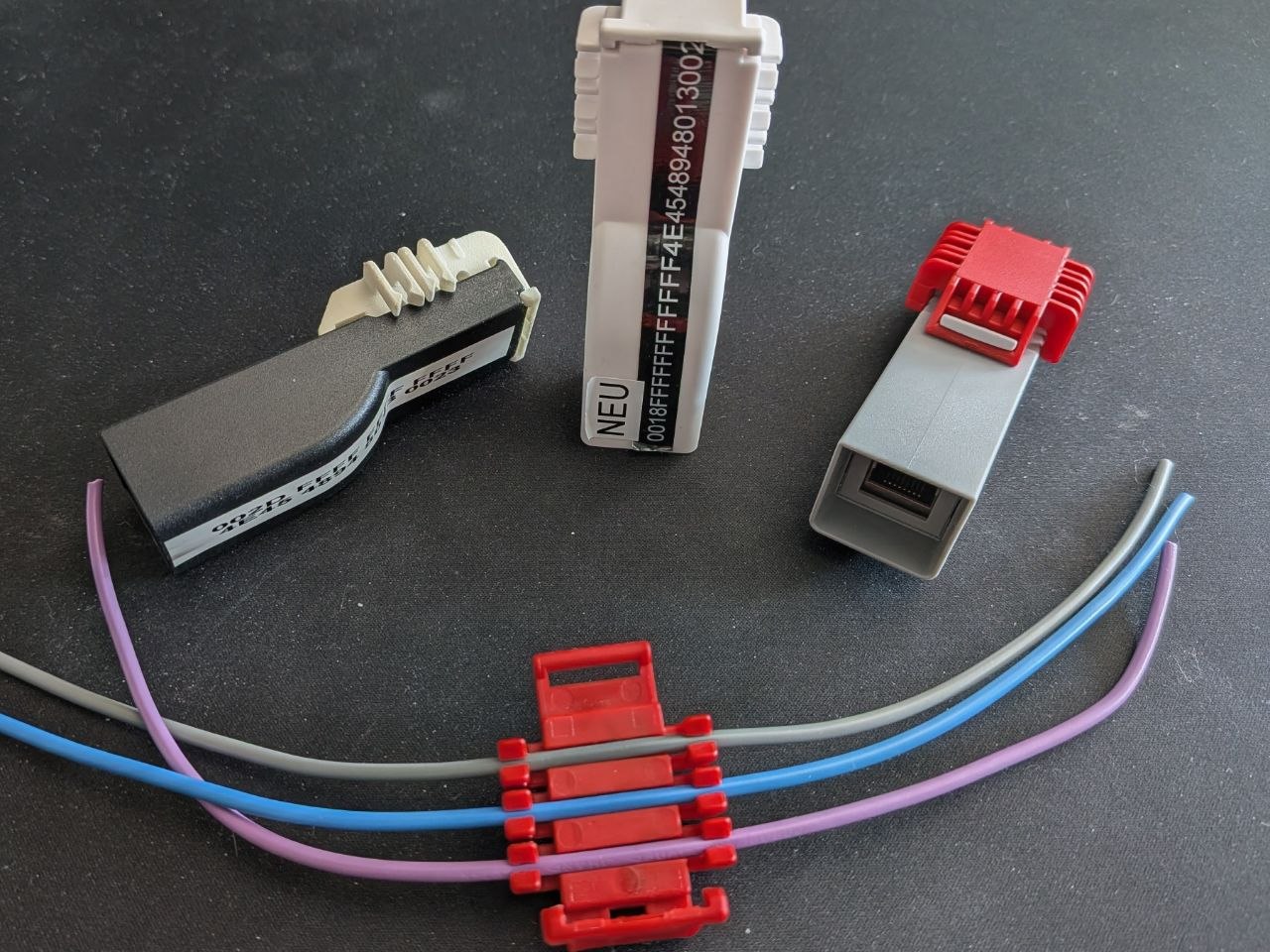 Three generations of housing (left to right: early black prototype, tall white variant, final grey enclosure with red locking clip and RJ45 port) alongside the ferrite-embedded clamping mechanism for the three-phase conductors.
